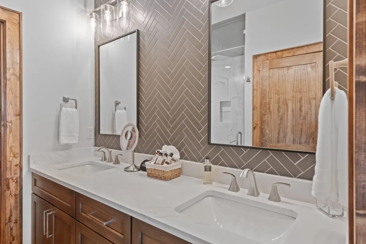A modern bathroom with a spacious double vanity, elegant herringbone backsplash, mirrored cabinets, and wooden accents. The space is bathed in soft, natural light, creating a spa-like ambiance that exudes both sophistication and relaxation.