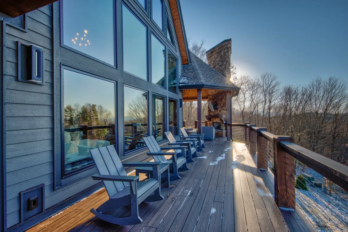 An inviting exterior deck features comfortable seating, a cozy outdoor fireplace, and large windows that reveal the natural surroundings. The scene captures the ideal spot for unwinding with friends, sharing drinks, and enjoying sunset moments outdoors.