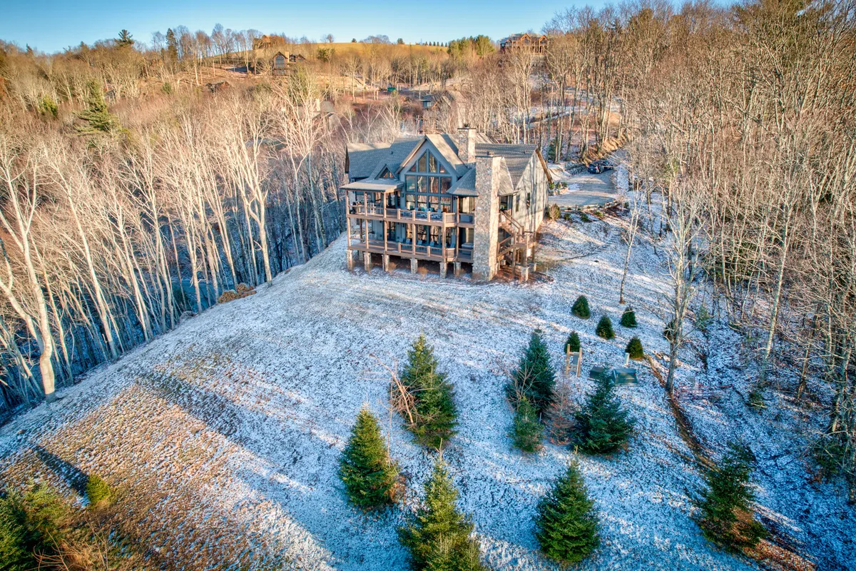 This exterior image features the large house surrounded by trees and a snow-covered ground, capturing the tranquil setting of Eagles Nest in winter. The scene evokes a sense of peacefulness and showcases the natural environment as well as space for family gatherings and outdoor barbecues.