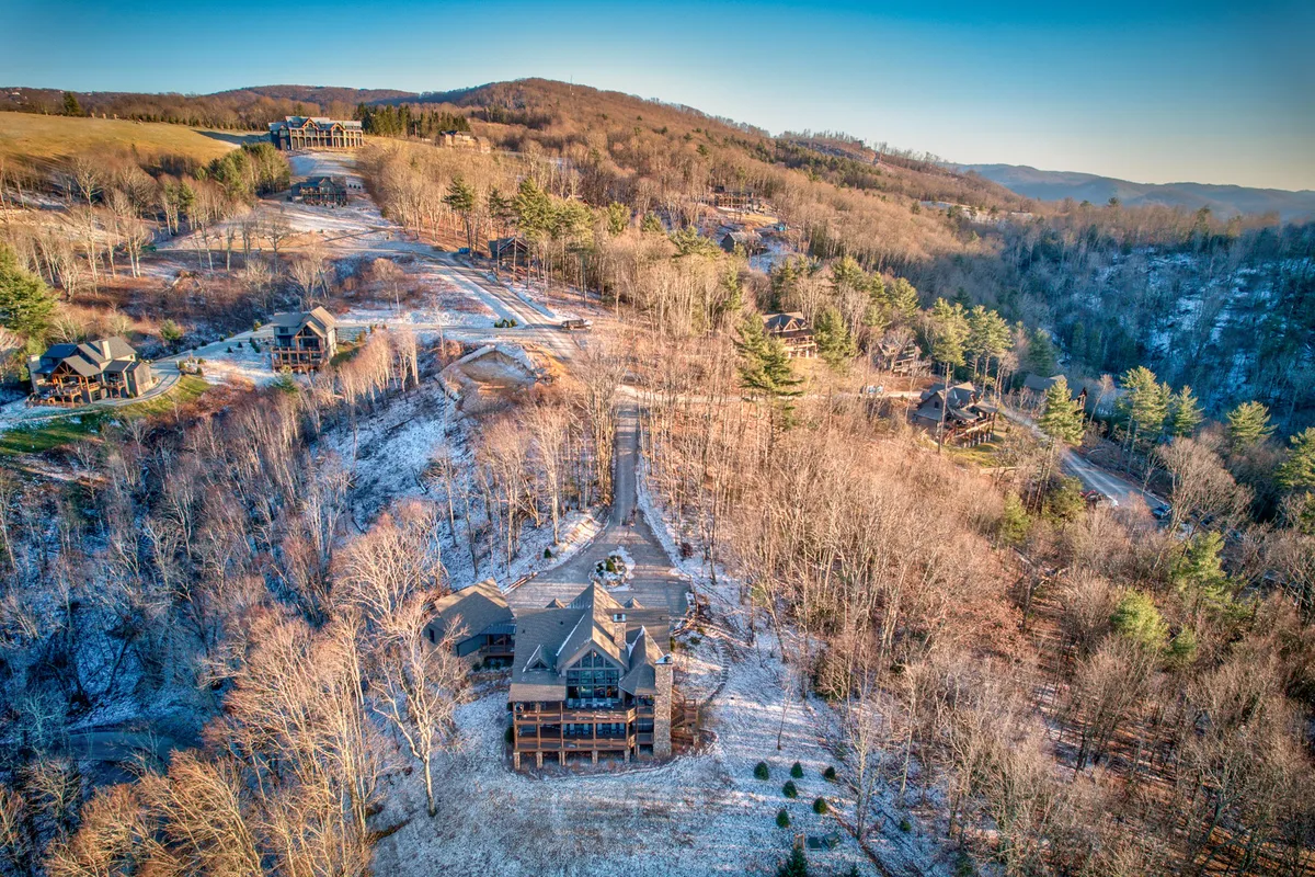 This exterior image showcases a spacious home nestled within the natural beauty of the Blue Ridge, with a winding road, lush trees, and a distant mountain range. The setting captures families gathering outdoors, with room for hiking and exploring the surrounding landscape.