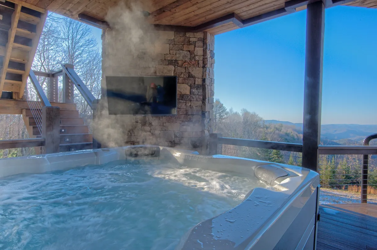 A cozy indoor hot tub area with mountain views and a wall-mounted television. Stone walls add a rustic touch, and the room feels like a relaxing escape that connects seamlessly to the outdoors.