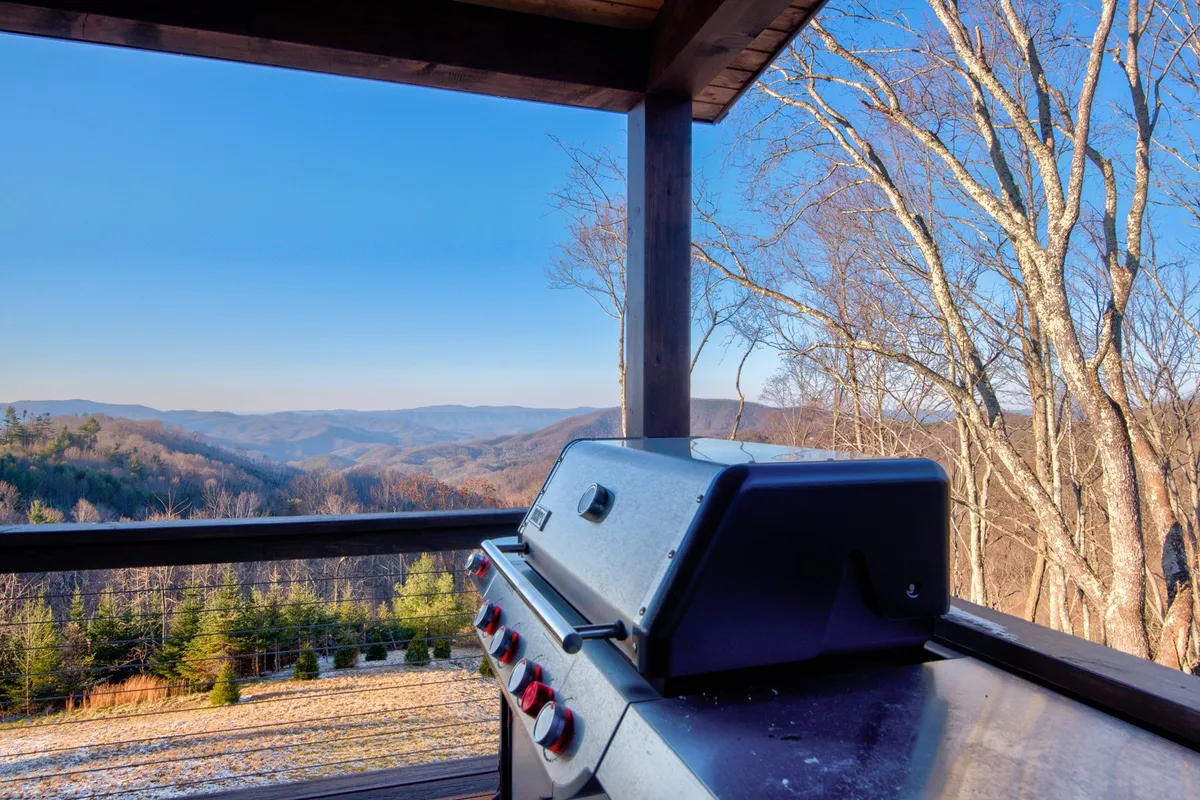 A portion of the deck with a grill positioned for outdoor cooking, mountain views visible through the railing, and a relaxed, open-air atmosphere ideal for alfresco dining or sunset barbecues.